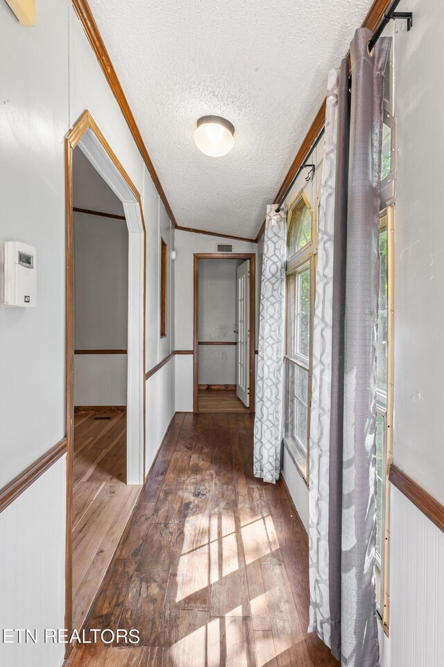 corridor featuring dark wood-type flooring, a textured ceiling, and ornamental molding