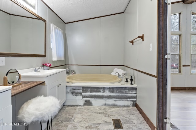 bathroom with a textured ceiling, vanity, crown molding, and a tub