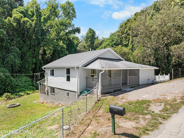 view of front of home with driveway, roof with shingles, covered porch, fence, and a front yard