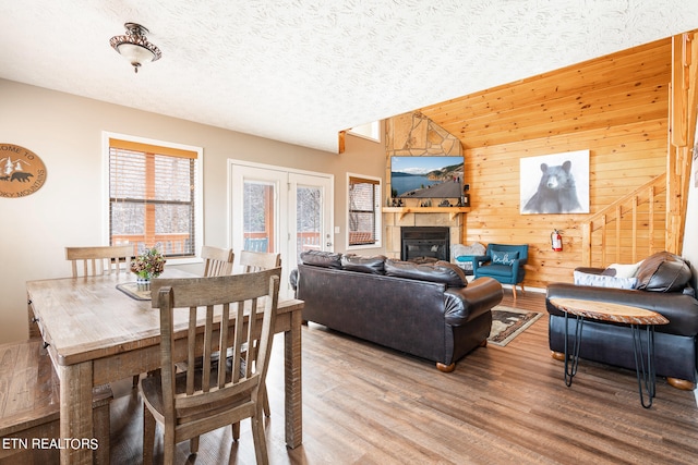 dining space with hardwood / wood-style floors, french doors, a textured ceiling, wooden walls, and lofted ceiling