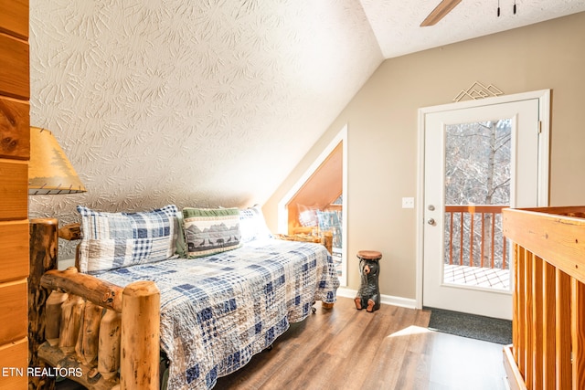 bedroom with ceiling fan, wood-type flooring, vaulted ceiling, access to exterior, and a textured ceiling