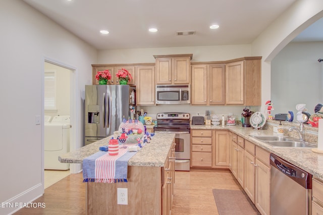 kitchen with light hardwood / wood-style flooring, sink, appliances with stainless steel finishes, washing machine and dryer, and light brown cabinetry