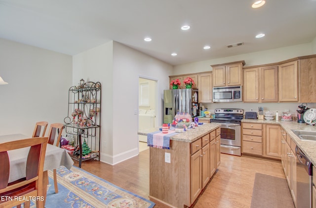 kitchen featuring appliances with stainless steel finishes, light brown cabinets, light stone countertops, light hardwood / wood-style flooring, and a center island