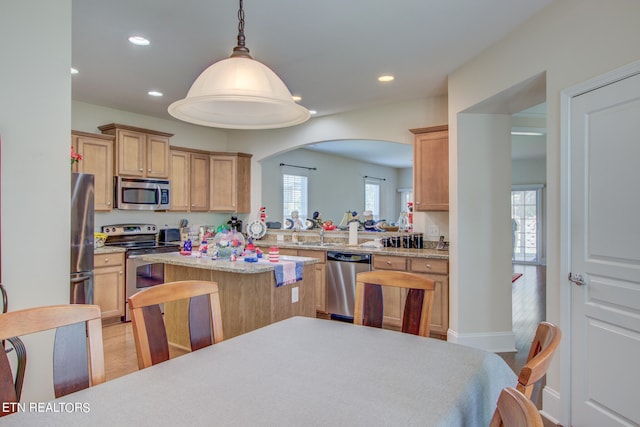 kitchen with light hardwood / wood-style floors, kitchen peninsula, appliances with stainless steel finishes, a kitchen breakfast bar, and hanging light fixtures