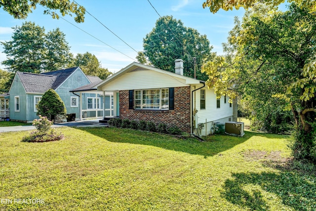 view of front of property with central air condition unit, a chimney, a front lawn, and brick siding