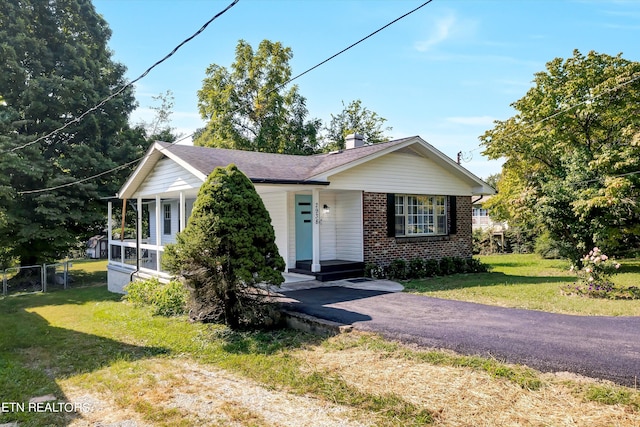 view of front facade with brick siding, roof with shingles, a chimney, driveway, and a front lawn