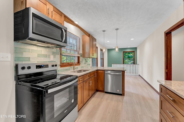 kitchen featuring brown cabinets, decorative light fixtures, a peninsula, stainless steel appliances, and a sink