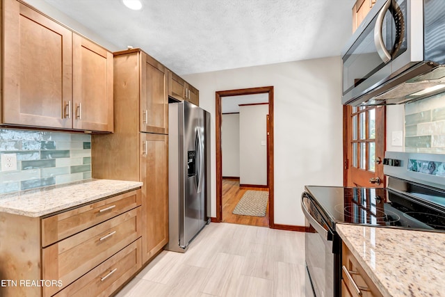 kitchen featuring light stone counters, decorative backsplash, appliances with stainless steel finishes, a textured ceiling, and baseboards