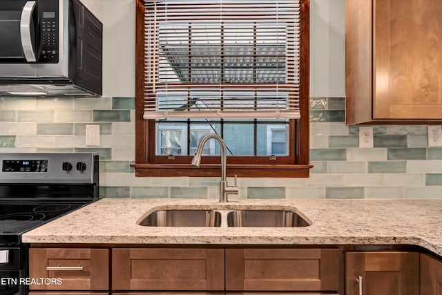 kitchen with stainless steel appliances, brown cabinets, a sink, and light stone counters