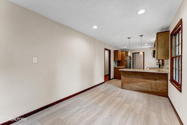 kitchen with pendant lighting, appliances with stainless steel finishes, brown cabinetry, a sink, and a peninsula