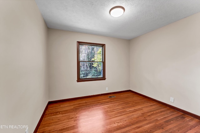 spare room featuring baseboards, a textured ceiling, visible vents, and wood finished floors