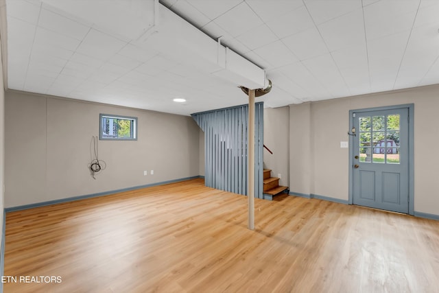 below grade area with light wood finished floors, baseboards, stairway, and a wealth of natural light