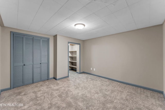 unfurnished bedroom featuring baseboards, crown molding, a closet, and light colored carpet