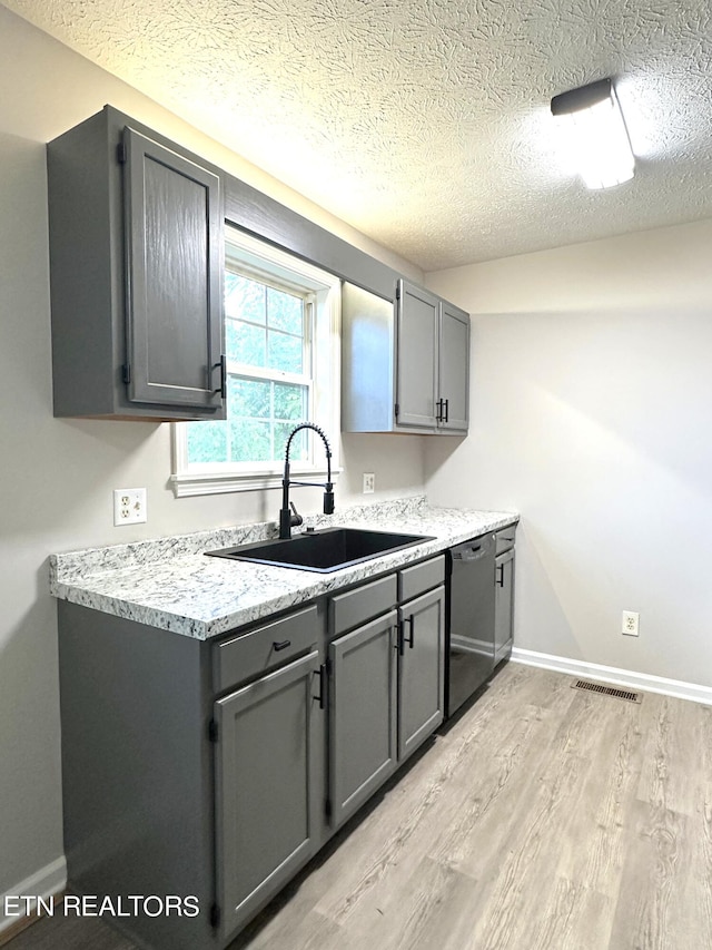 kitchen with a textured ceiling, light hardwood / wood-style flooring, sink, stainless steel dishwasher, and gray cabinetry