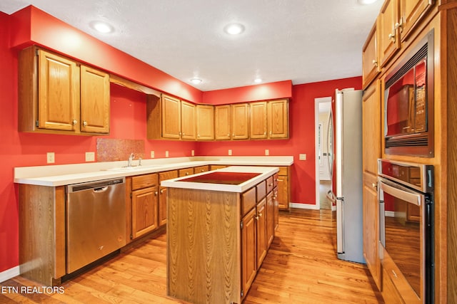 kitchen featuring stainless steel appliances, light wood-type flooring, a textured ceiling, a center island, and sink