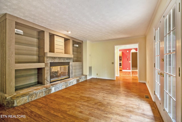 unfurnished living room with french doors, light hardwood / wood-style floors, a fireplace, and a textured ceiling