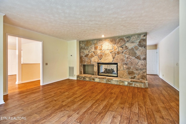 unfurnished living room featuring wood-type flooring, a stone fireplace, a textured ceiling, and crown molding