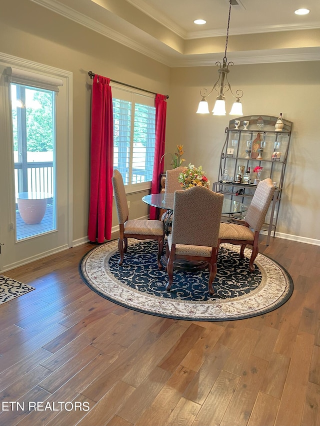 dining space with ornamental molding, a raised ceiling, baseboards, and hardwood / wood-style flooring