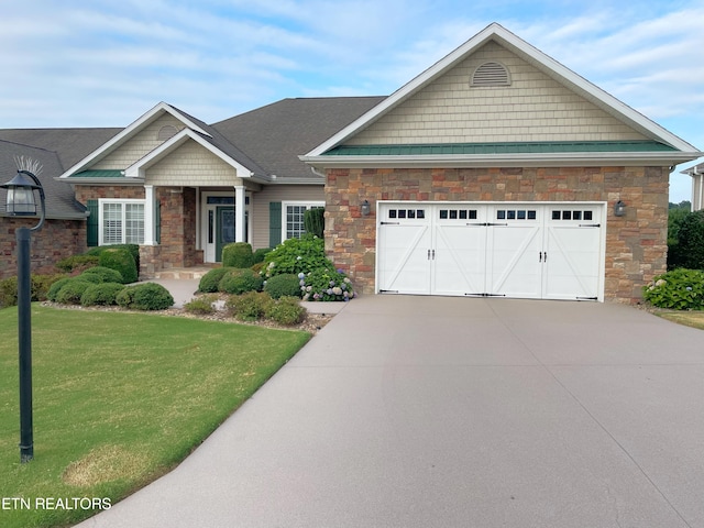 craftsman-style house featuring a garage, driveway, stone siding, and a front yard