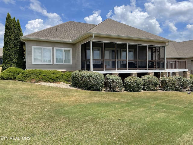 rear view of property featuring a sunroom, roof with shingles, and a lawn