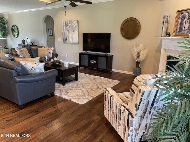 living area with arched walkways, a fireplace, dark wood finished floors, ornamental molding, and baseboards