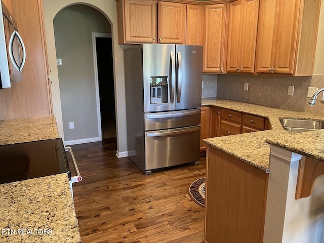 kitchen featuring light stone countertops, a sink, appliances with stainless steel finishes, decorative backsplash, and dark wood finished floors