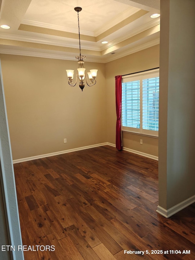 spare room featuring dark wood-style flooring, a notable chandelier, crown molding, a raised ceiling, and baseboards