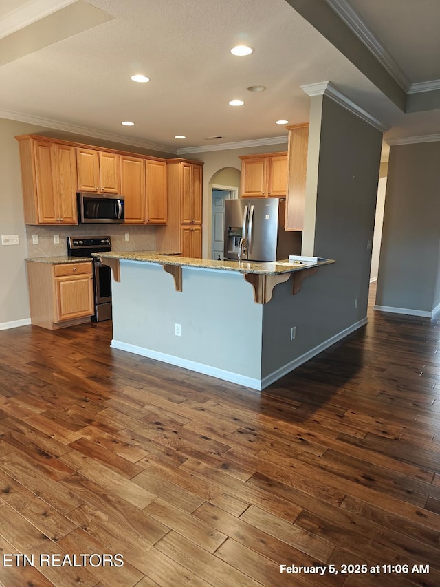 kitchen featuring arched walkways, a kitchen breakfast bar, dark wood-style flooring, stainless steel appliances, and backsplash