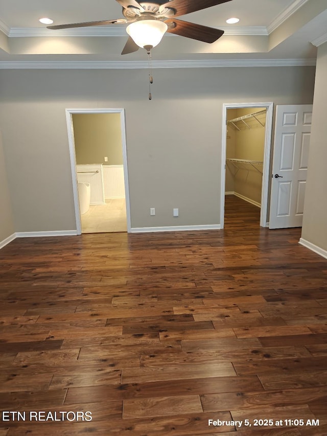 unfurnished bedroom featuring a walk in closet, dark wood-style flooring, crown molding, and baseboards