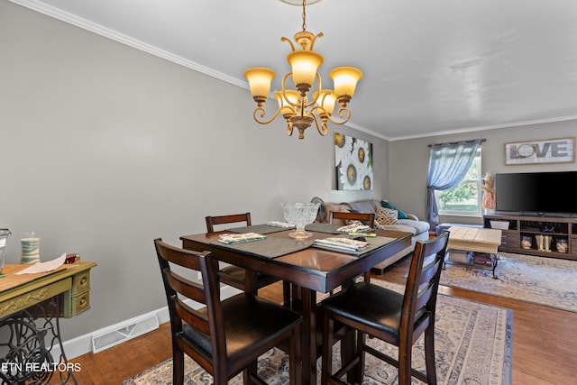 dining room with hardwood / wood-style flooring, ornamental molding, and an inviting chandelier