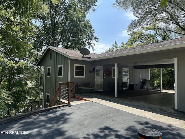 rear view of property featuring board and batten siding, roof with shingles, and a carport