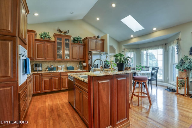 kitchen featuring light stone countertops, a kitchen island with sink, stainless steel appliances, a skylight, and light wood-type flooring