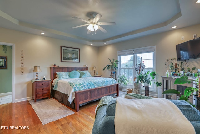 bedroom with a tray ceiling, ceiling fan, and light hardwood / wood-style flooring