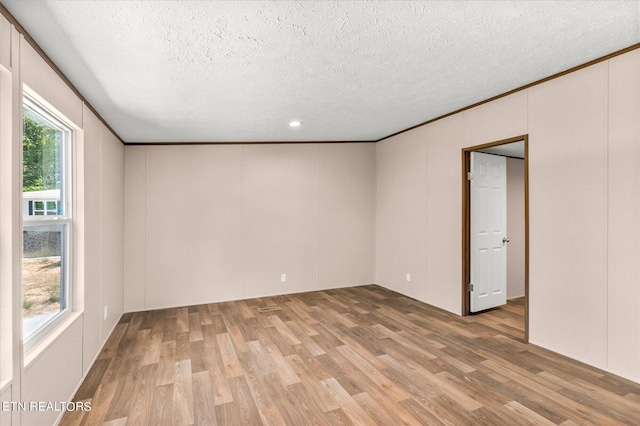 empty room featuring light wood finished floors, a decorative wall, a textured ceiling, and crown molding