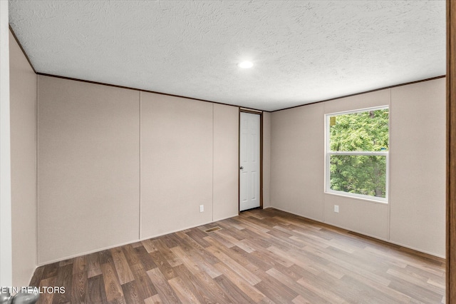 empty room with light wood-style flooring, ornamental molding, and a textured ceiling