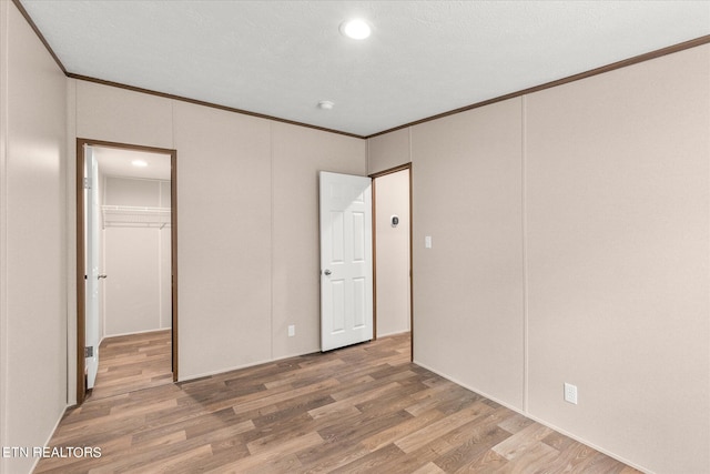 unfurnished bedroom featuring a spacious closet, crown molding, a closet, and wood finished floors