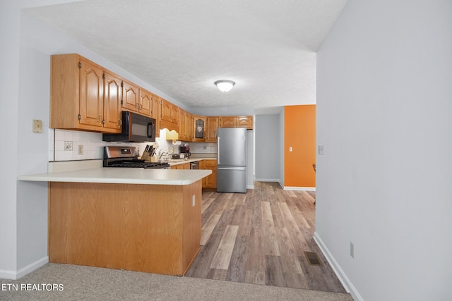 kitchen with a textured ceiling, backsplash, light hardwood / wood-style floors, stainless steel appliances, and kitchen peninsula