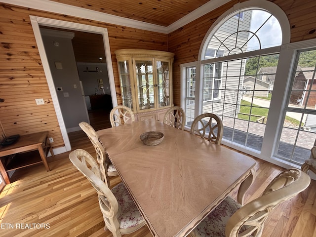 dining space featuring ornamental molding, wooden walls, and light wood finished floors