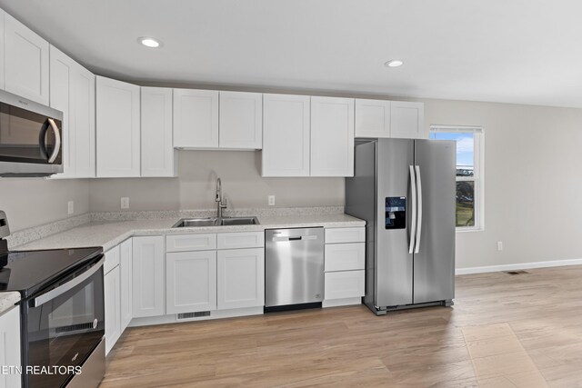 kitchen with sink, appliances with stainless steel finishes, white cabinets, and light hardwood / wood-style floors