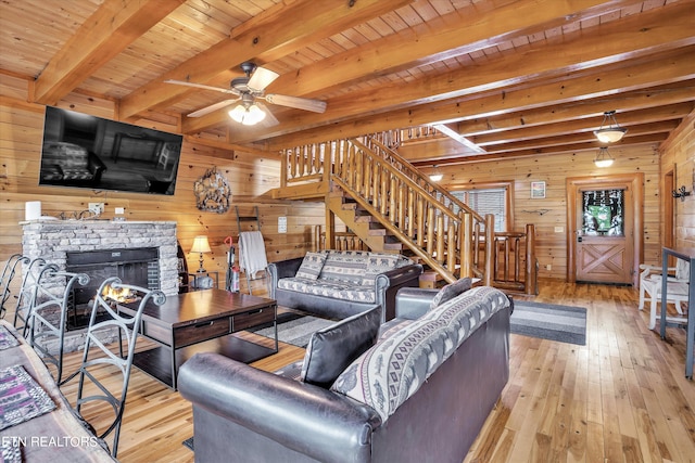 living room with light hardwood / wood-style flooring, wood walls, ceiling fan, a stone fireplace, and wood ceiling