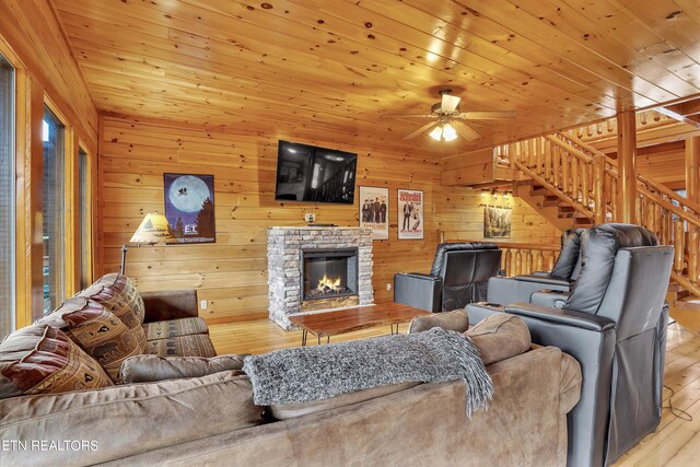 living room featuring a fireplace, wooden ceiling, light hardwood / wood-style flooring, wood walls, and ceiling fan