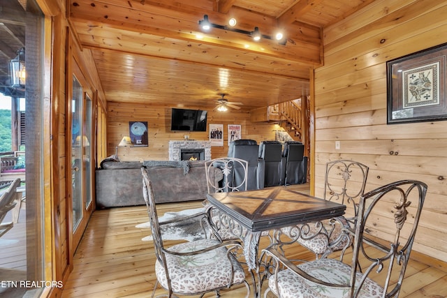 dining space with ceiling fan, a fireplace, beam ceiling, and light hardwood / wood-style flooring