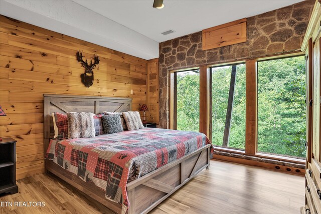 bedroom with wood walls, multiple windows, and hardwood / wood-style flooring