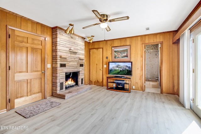 unfurnished living room featuring a fireplace, wooden walls, a healthy amount of sunlight, light hardwood / wood-style floors, and ceiling fan