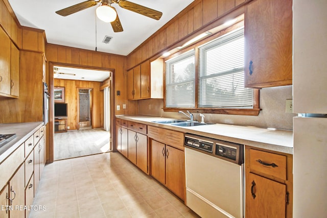 kitchen featuring ceiling fan, white dishwasher, wooden walls, and sink