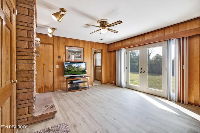 unfurnished living room with light hardwood / wood-style flooring, ceiling fan, wooden walls, and french doors