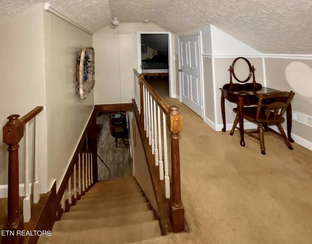 stairway featuring lofted ceiling, carpet, and a textured ceiling