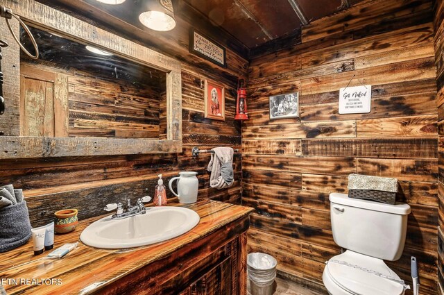 bathroom with wood walls, toilet, and vanity