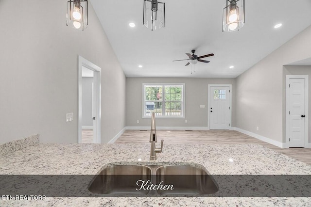 kitchen with lofted ceiling, light stone counters, decorative light fixtures, and sink