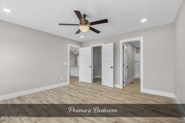 unfurnished bedroom with a spacious closet, a closet, light wood-type flooring, and ceiling fan